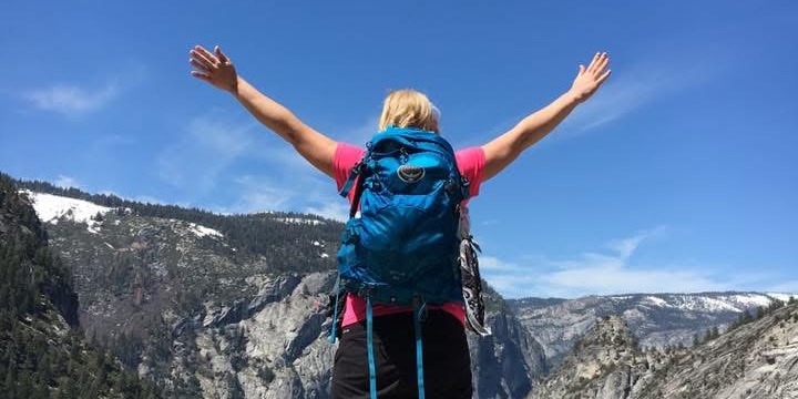 Tiffany standing on a granite outcrop in Yosemite National Park with arms raised, overlooking the valley